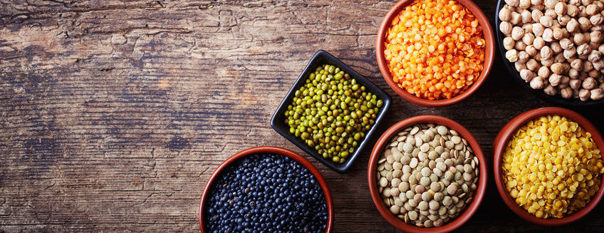 Bowls of various legumes (chickpeas, green peas, red lentils, canadian lentils, indian lentils, black lentils, green lentils; yellow peas, green mung beans) on wooden background